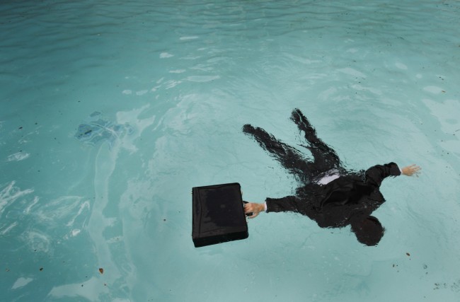 Business man with briefcase floating face down in pool